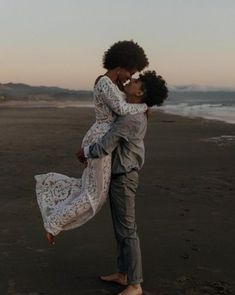 a man and woman hugging on the beach at sunset with waves in the background,