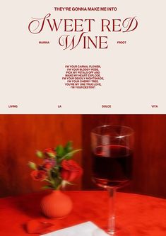 there is a glass of red wine on the table with a napkin and flower vase