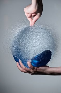 two hands are sprinkled with water from a blue ball that is being held by another hand