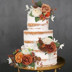 a three tiered cake with flowers and leaves on the top is sitting on a gold stand