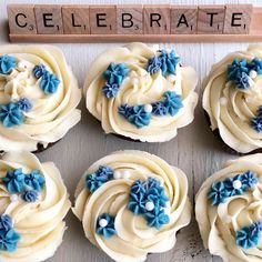 six cupcakes with white frosting and blue flowers are arranged on a table