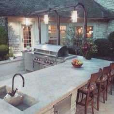 an outdoor kitchen with grill, sink and bar stools in front of the house