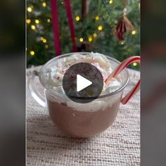 a cup filled with whipped cream and candy canes on top of a table next to a christmas tree