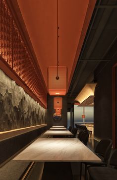 a long table with black chairs in front of an orange wall and some lights hanging from the ceiling