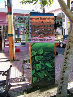 there is a sign on the sidewalk in front of a building with trees and benches