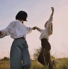 two people standing on top of a grass covered field next to each other with their arms in the air