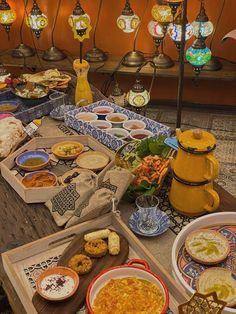 an assortment of food is displayed on a long table with lights in the back ground