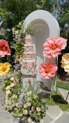 a wedding cake is surrounded by flowers and greenery in front of a white arch