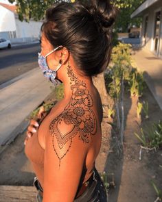 a woman with a tattoo on her back is standing in front of a tree and some bushes