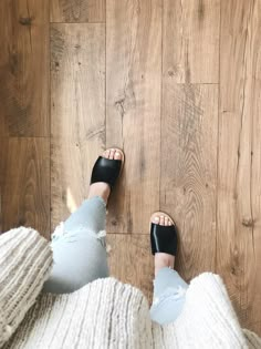 a person standing on top of a wooden floor next to a pair of black sandals