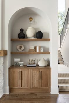 a wooden shelf with vases and books on it in front of a stair case