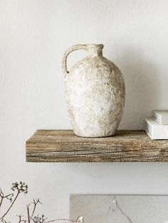 a white vase sitting on top of a wooden shelf next to a book and plant