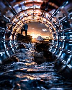 a man standing on top of a rock next to the ocean in a metal tunnel