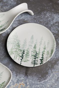 two plates with trees painted on them are sitting next to each other in front of a gray background