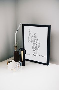 a white desk topped with a framed drawing next to a pair of scissors and a cup