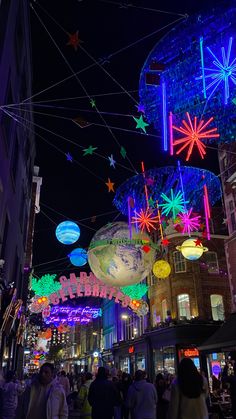 people walking down the street at night with colorful lights and decorations hanging from the ceiling