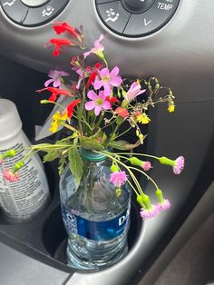 a vase with flowers in it sitting on the dash board next to a bottle of water