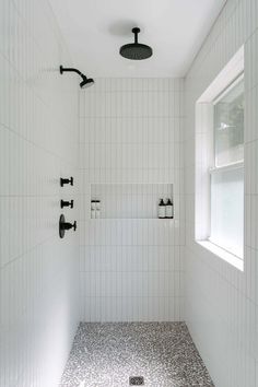 a white tiled bathroom with black and white tile on the shower head, window, and faucet