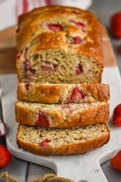 sliced loaf of strawberry banana bread sitting on top of a cutting board next to strawberries