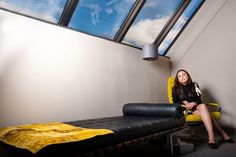 a woman sitting in a chair next to a bed with a skylight above it