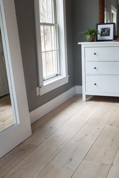 a white dresser sitting in front of a window next to a mirror on top of a wooden floor