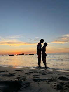 two people standing on the beach at sunset with their arms around each other and kissing