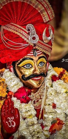 a man wearing a red turban and gold face paint with flowers around his neck