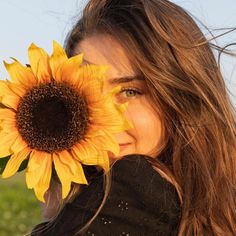 a woman with long hair holding a sunflower in front of her face and looking at the camera