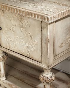 an old white cabinet with ornate carvings on the front and sides, sitting on a wooden floor