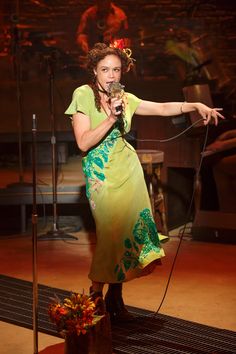 a woman in a green dress is holding a microphone and standing on a stage with her hand out