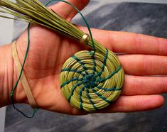 a hand holding a piece of string wrapped in green and brown yarn with a knot around it