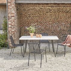 two chairs and a table in front of a brick wall with potted plants on it