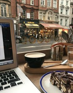 a laptop computer sitting on top of a table next to a cup of coffee and cake