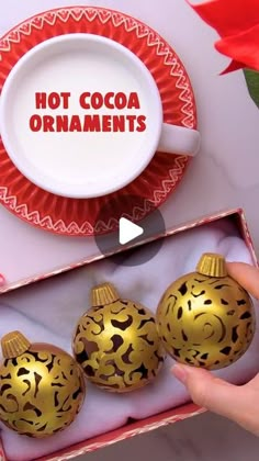 someone is holding three ornaments in a box with the words hot cocoa ornaments on it