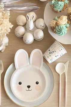 a table topped with plates and cupcakes covered in frosted bunny face decorations