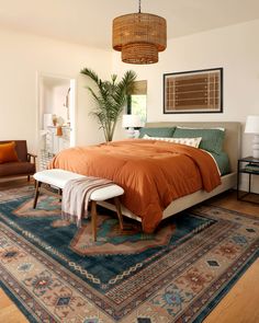 a bed with an orange comforter on top of it in a bedroom next to a chair