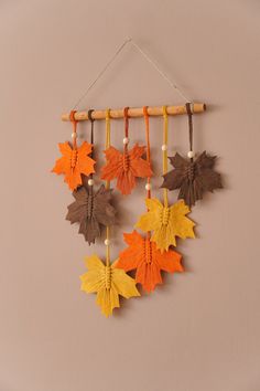 an orange and brown fall leaf mobile hangs on a wall next to a wooden stick