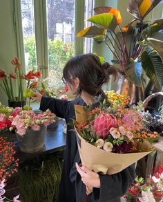 a woman holding a bouquet of flowers in front of a table with potted plants