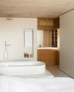 a bath tub sitting next to a white bed in a bathroom under a wooden ceiling