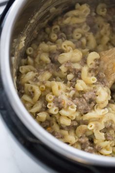 a pot filled with macaroni and cheese sitting on top of a stove next to a wooden spoon