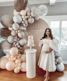 a woman standing in front of a cake and balloon arch with the words baby shower written on it