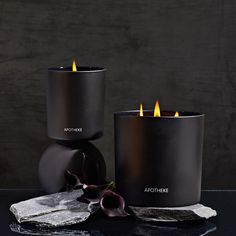 two black candles sitting next to each other on top of a table with an orchid