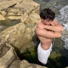 a man standing in the water next to some rocks and holding his hands on his chest