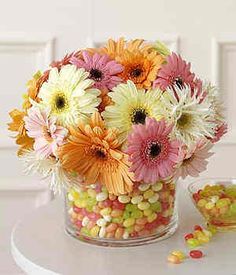 a glass vase filled with candy corn and colorful flowers on top of a white table