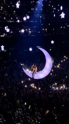 a person standing on top of a crescent moon in the middle of a stage filled with people