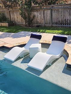 two white lounge chairs sitting on top of a swimming pool