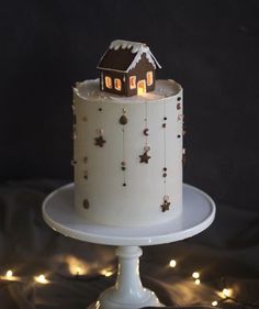 a white cake topped with a small house on top of a table covered in lights