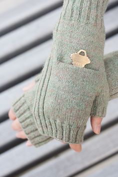 a person's hand wearing green mitts with a gold heart on it and a pair of fingerless gloves