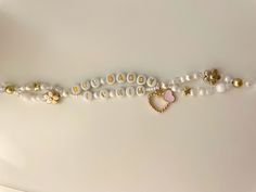 a white necklace with gold charms and pearls on the bottom, along with a heart - shaped brooch