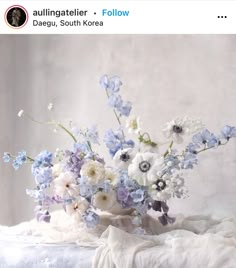 a vase filled with lots of white and blue flowers on top of a table next to a wall